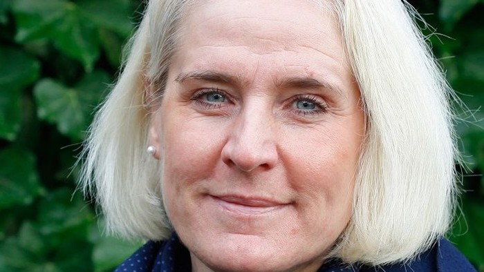 Frau mit blondem Haar und blauem Schal vor grünem Hintergrund