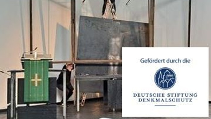Eine Person reinigt ein großes Steinmonument in einem modernen architektonischen Umfeld mit vermerkter Erhaltungssponsorschaft.