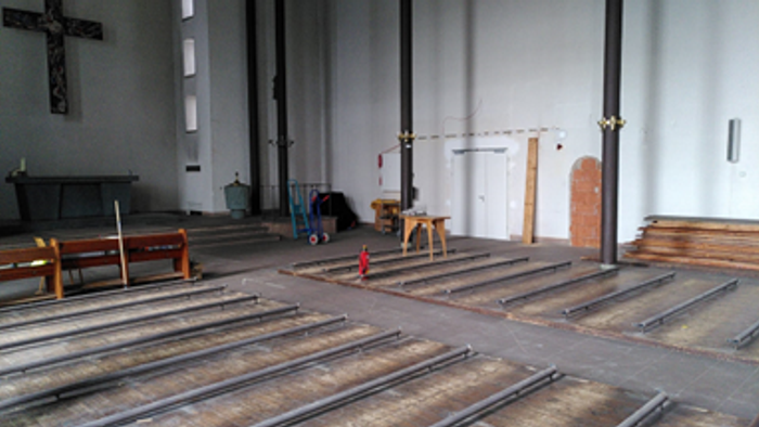 Kircheninneres mit hölzernen Kirchenbänken und einem Kreuz an der Wand.