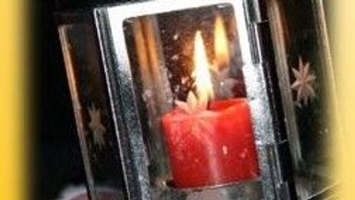 Eine Hand hält eine silberne Laterne mit einer brennenden roten Kerze.