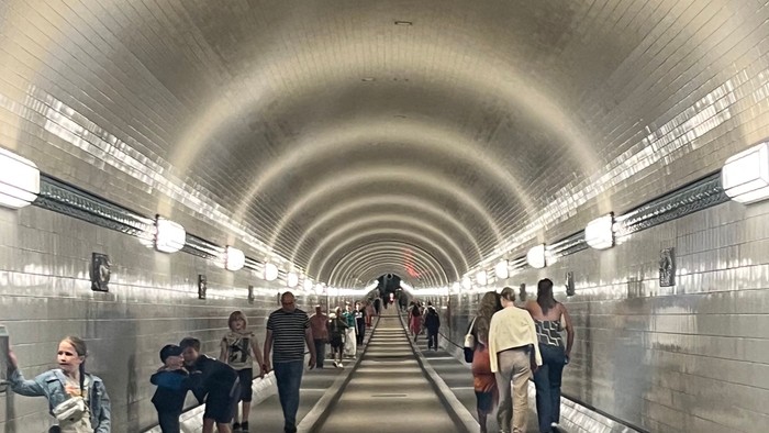 Menschen gehen durch einen beleuchteten Tunnel mit Gleisen.