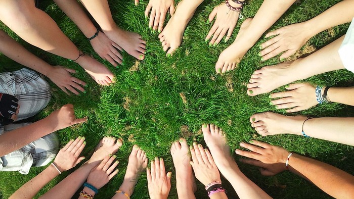 En gruppe af mennesker sidder i en kreds med håndene udstrakt mod midten på en græsplæne