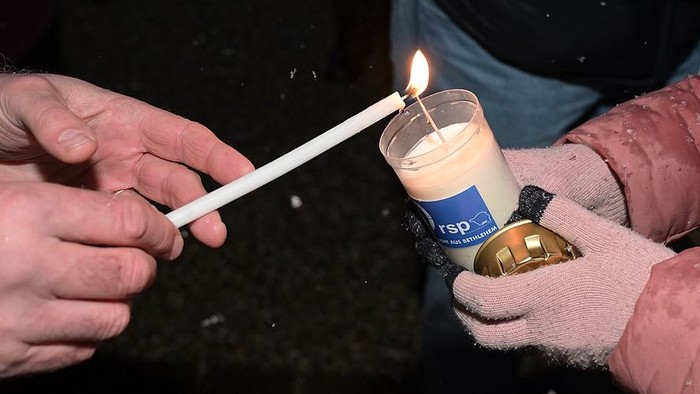 Zwei Personen zünden eine Kerze an, eine trägt Handschuhe