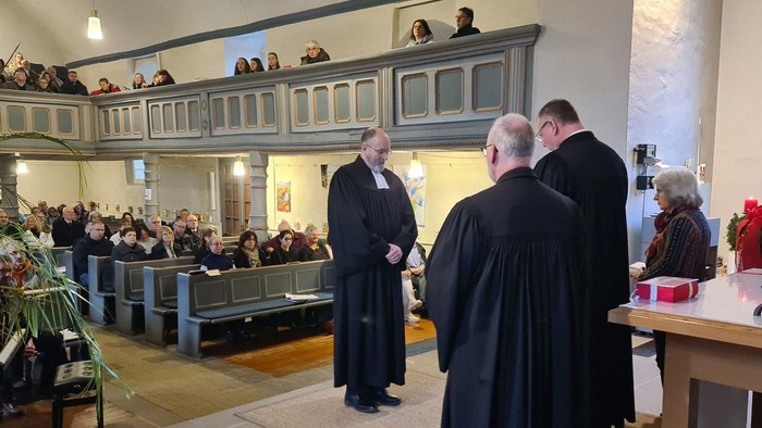 Eine Gruppe von Priestern steht vor einer Kirchenbank, während eine Menschenmenge zusieht.