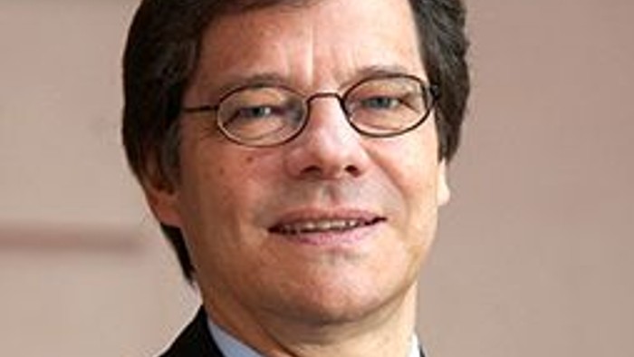 Ein Mann mit Brille und Krawatte lächelt in die Kamera.