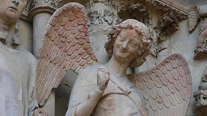 Zwei Steinfiguren, eine mit Flügeln, vor einem Gebäude.