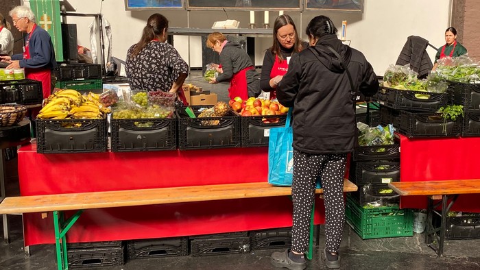 Gemeinschaftliche Lebensmittelverteilung mit Freiwilligen, die frische Produkte an Besucher in einem geräumigen Innenbereich ausgeben.