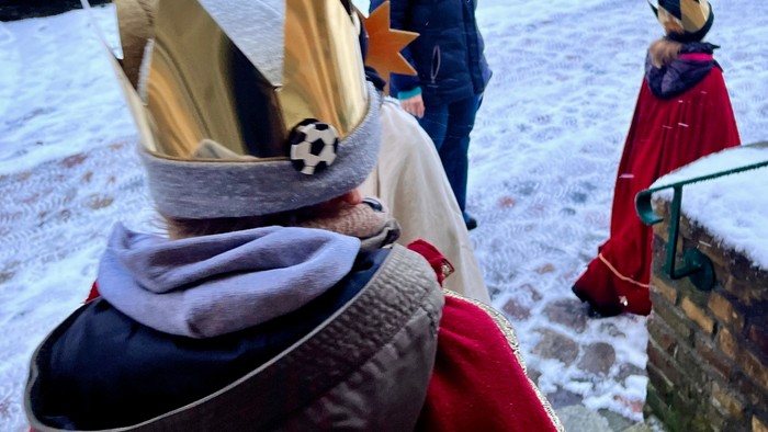 Menschen in festlicher Tracht mit traditionellen Hüten und Gewändern stehen bei Schneewetter im Freien.