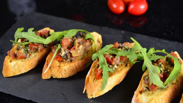 Fire smørbrød med grønne blad og tomater på sort brød.