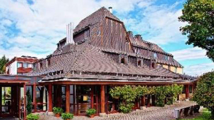 Elegante Holzhütte mit Kopfsteinpflaster-Einfahrt, umgeben von üppigem Grün und Topfpflanzen.