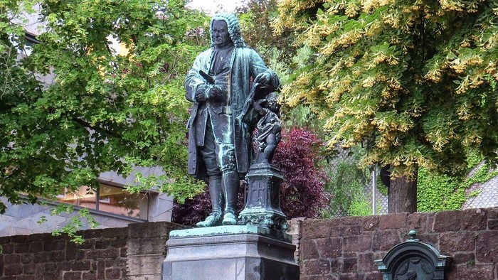 En bronze statue af en mand med bog og pen, placeret på en sokkel med indskrift.
