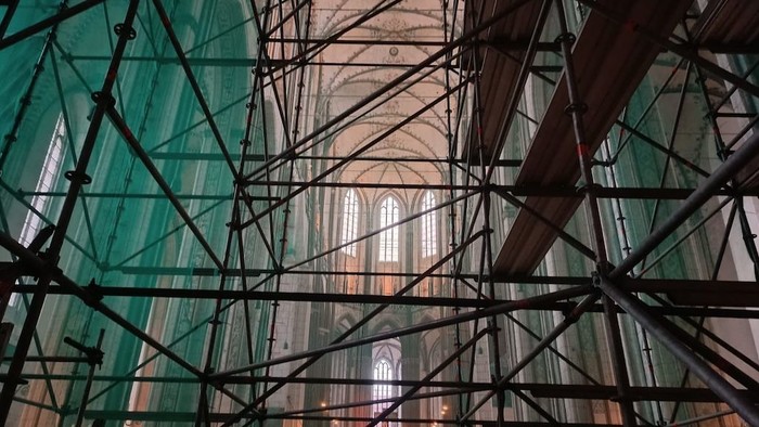 Gerüst im Inneren einer großen, prunkvollen Kathedrale mit hohen Gewölben und Buntglasfenstern.