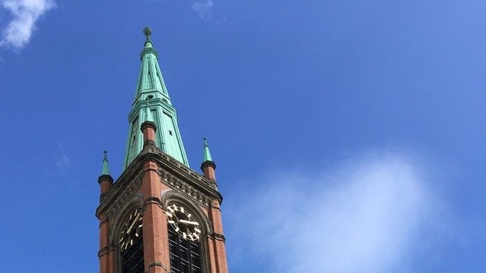 Der Kirchturm mit grünem Dach und Uhrwerk vor blauem Himmel