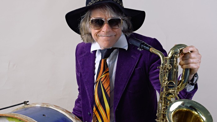 Ein Mann in lila Anzug und Cowboyhut spielt Saxophon und steht vor einer Bassdrum