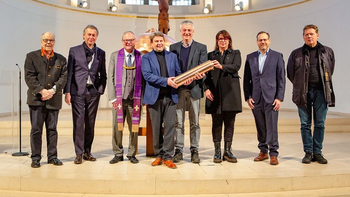 Eine Gruppe von Männern und einer Frau posiert in einem Kirchenraum, einer hält ein großes Buch