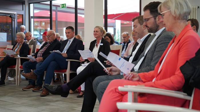Eine Gruppe von Menschen sitzt in einem Raum und hält Papiere in der Hand.