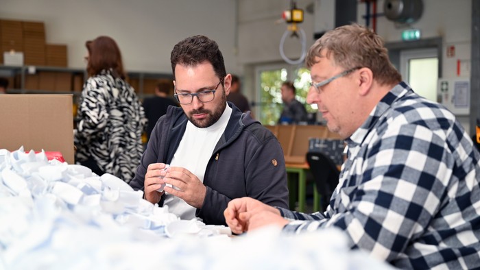 Zwei Männer arbeiten konzentriert an einem Tisch mit Papierstücken.