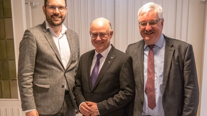 Drei Männer in Anzügen lächeln für ein Foto