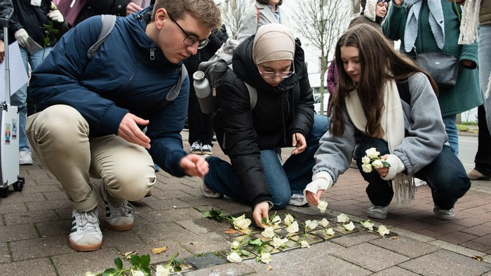 Drei junge Menschen knien auf dem Boden und legen Blumen nieder.