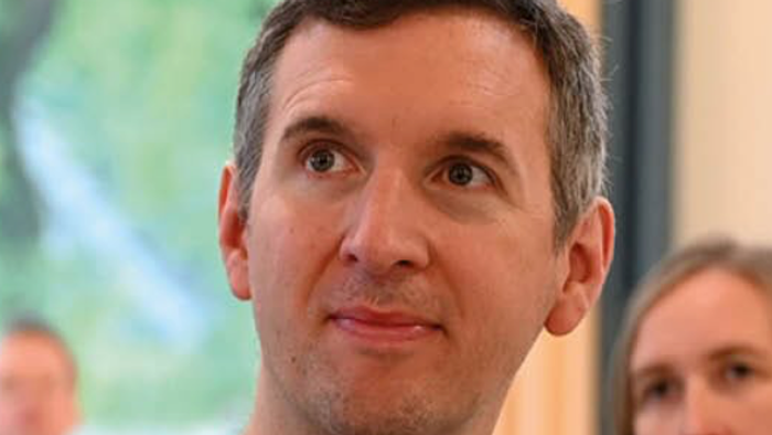 Mann mit grauen Pullover und Brille schaut in die Kamera.