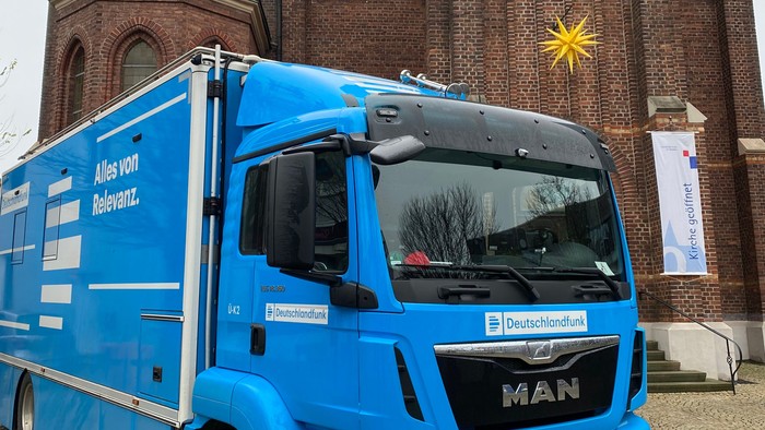 Blauer LKW vor historischer Kirche mit Uhrturm