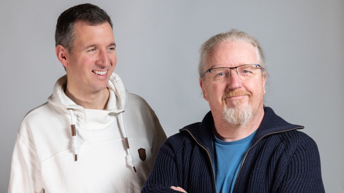 Zwei Männer stehen nebeneinander und lächeln in die Kamera