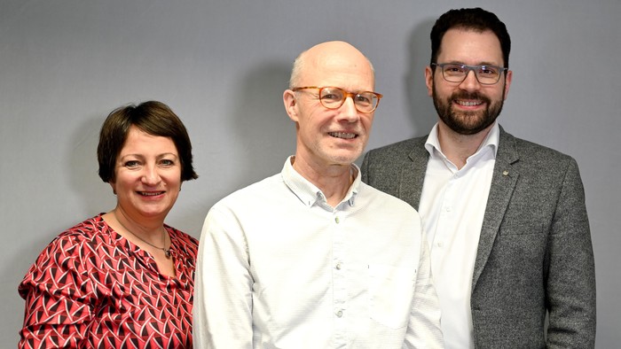 Drei Personen stehen nebeneinander und lächeln in die Kamera