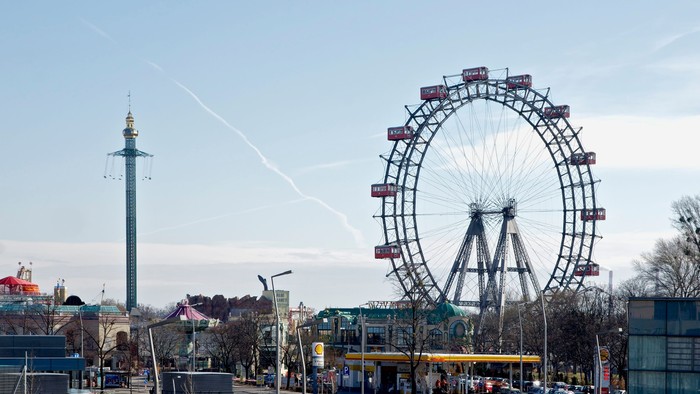 Im Bild ist ein Riesenrad und ein hoher Turm zu sehen, umgeben von Gebäuden und Bäumen.