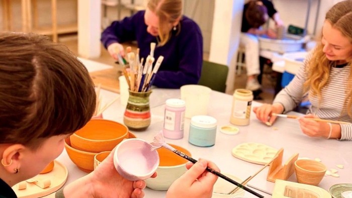 Folk maler keramikkrus under en workshop med forskellige malingfarver og pensler.