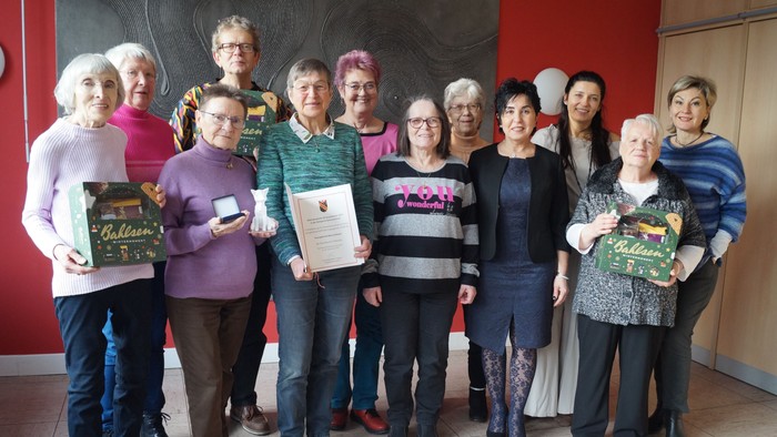 Eine Gruppe von Frauen, die gemeinsam posieren und Zertifikate sowie Geschenkkörbe in einem Flur halten.