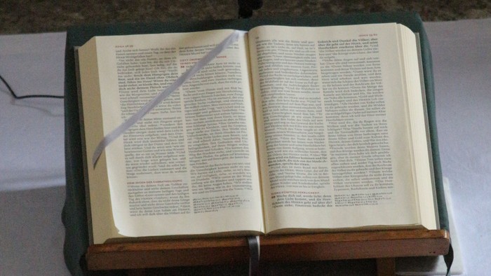 Offenes Buch auf Ständer mit roter Bibel daneben