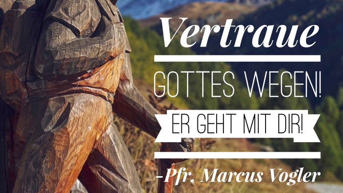 Holzstatue mit Bergkulisse und deutschem Text