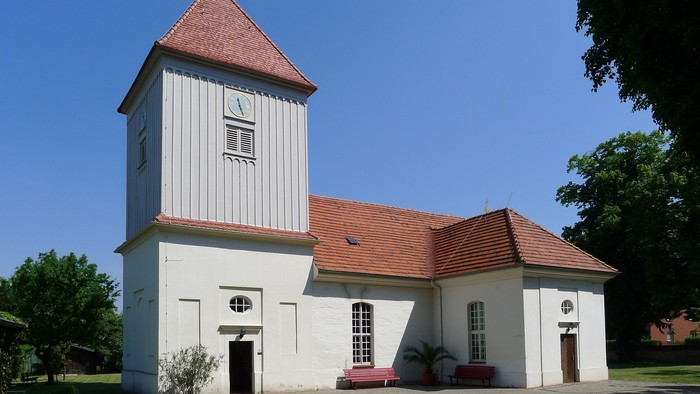 Weißes Kirchengebäude mit hohem Turm und roter Dachziegeln unter blauem Himmel