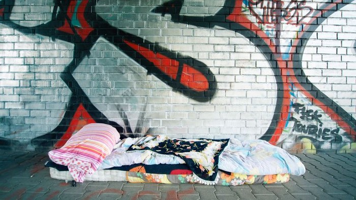 Ein Obdachloser schläft auf einer Decke vor einem Graffiti-Wand.