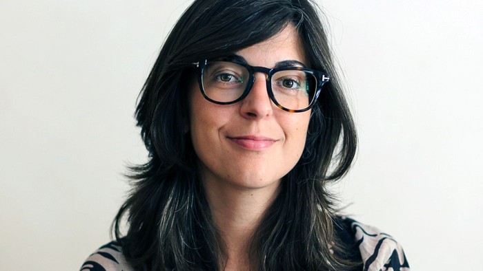 Eine Frau mit Brille und langem dunklem Haar lächelt in die Kamera.