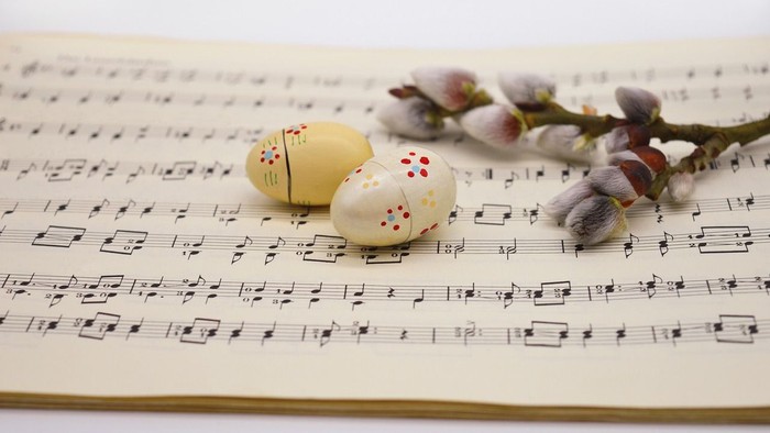 Zwei bemalte Ostereier und eine Blume liegen auf Notenblättern