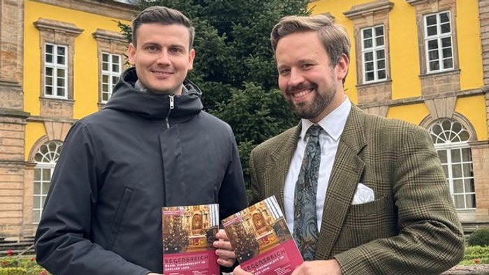 Zwei Männer halten Bücher vor einem gelben Gebäude.