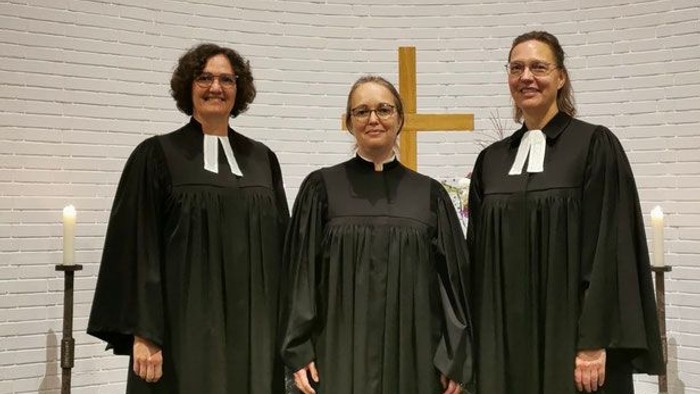Drei Frauen in schwarzen Gewändern und Kragen stehen gemeinsam in einer Kirche.