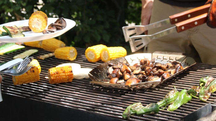 Zwei Personen grillen im Freien, verschiedene Lebensmittel auf dem Grill