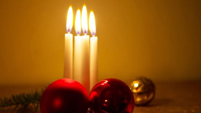 En lyse julelygte med tre lysende lys og to julekugler på bordet