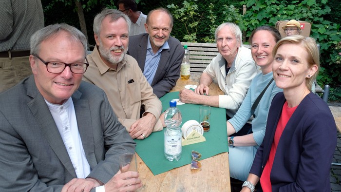 Eine Gruppe von sechs Personen sitzt an einem Tisch im Freien und genießt Getränke.