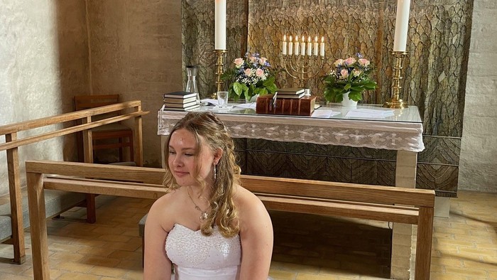 Kvinde i hvid kjole sidder i kirke.