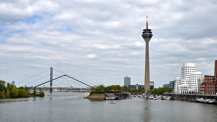 Der Rheinturm steht hoch neben dem Fluss mit Brücke und Booten.