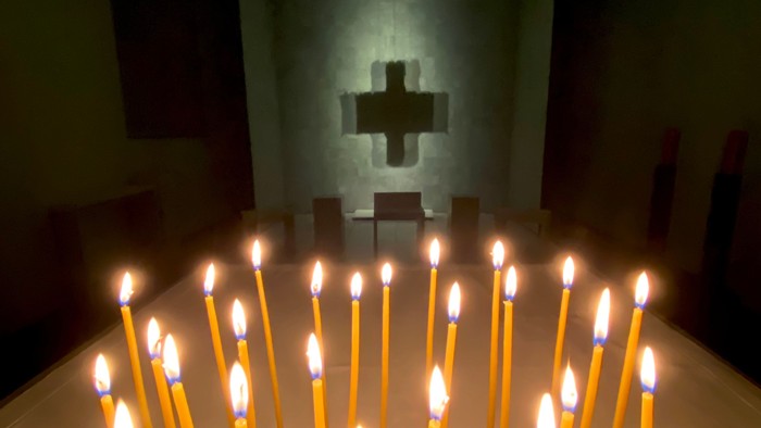 Viele brennende Kerzen vor einem Kreuz in einer Kirche