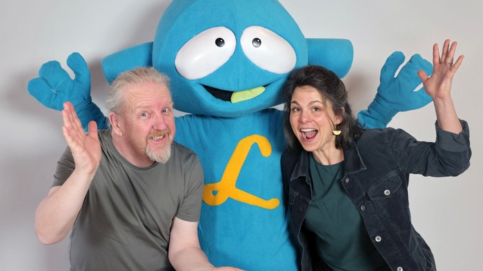 Ein Mann und eine Frau posieren mit einem blauen Maskottchen.