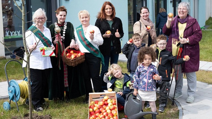 Eine Gruppe von Menschen, darunter Kinder, posiert mit Äpfeln und einem Baum.
