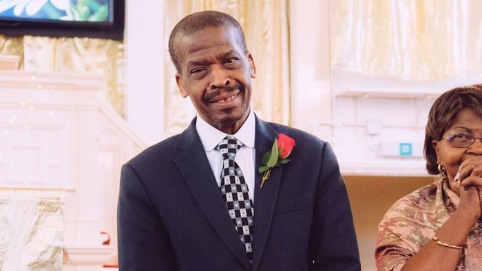 Man in suit with rose boutonniere smiles, woman beside him covers mouth.