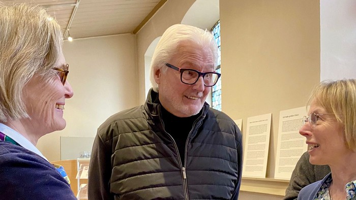 Drei ältere Menschen stehen in einem Raum und unterhalten sich.