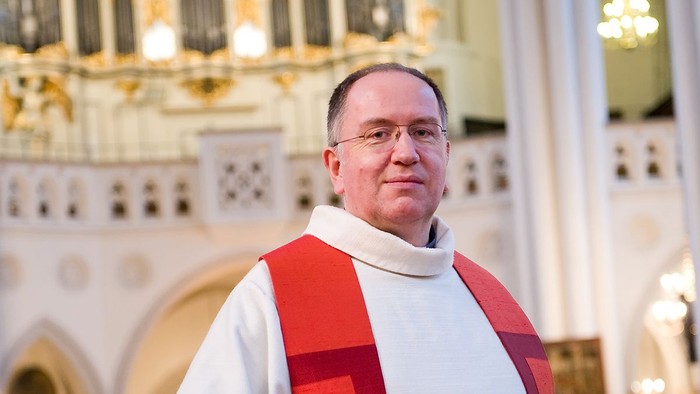 Ein Mann in kirchlicher Kleidung vor einem Kircheninneren.