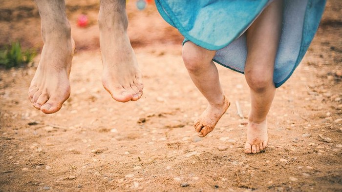Zwei Personen laufen barfuß am Strand, eine trägt ein blaues Handtuch.